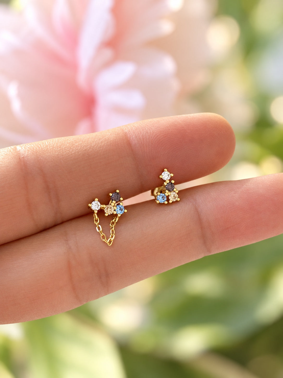Two asymmetrical multicolour gold studs on fingers for scale