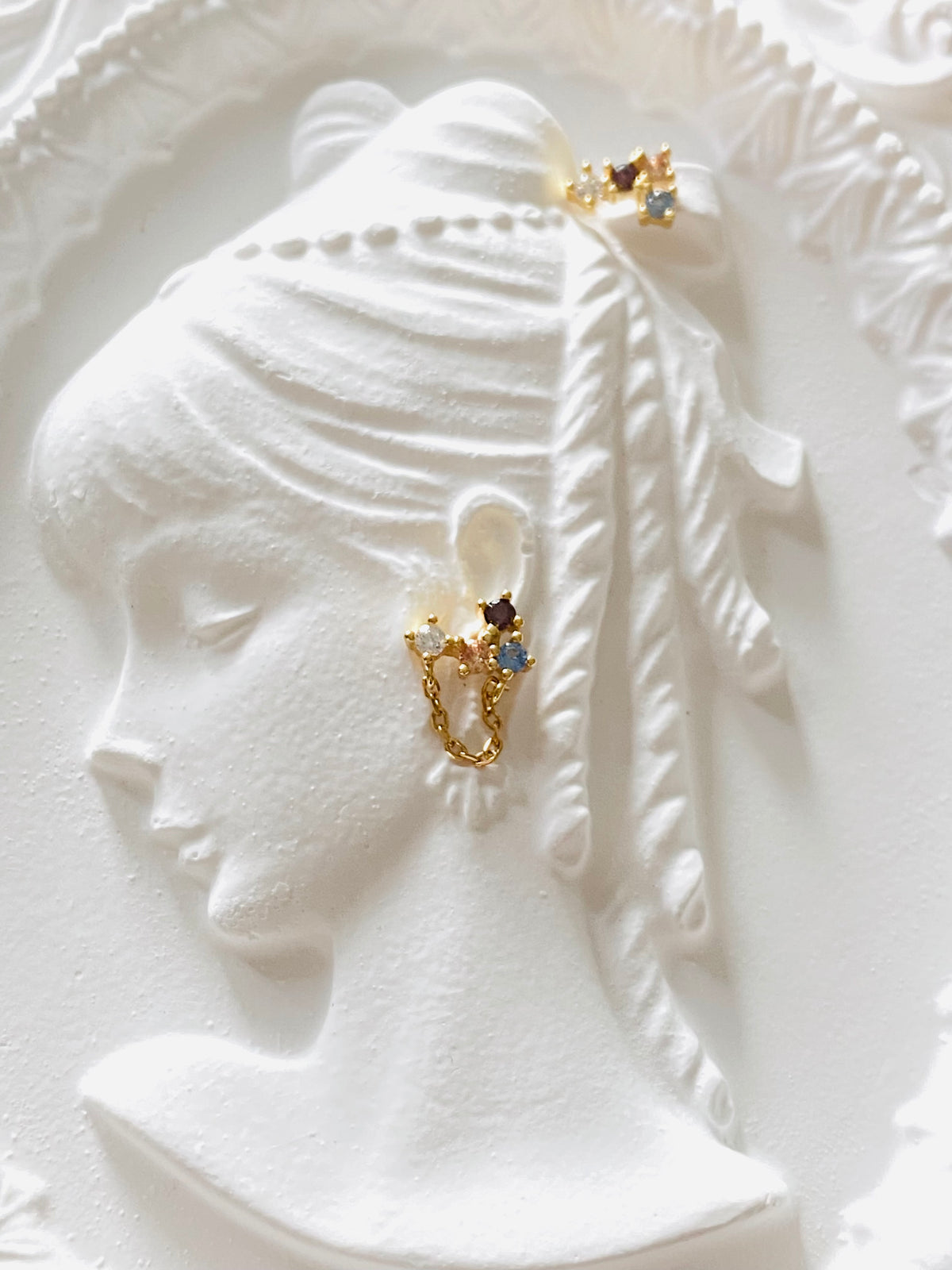 Asymmetric multicolour gold stud earrings on an ivory sculptural display