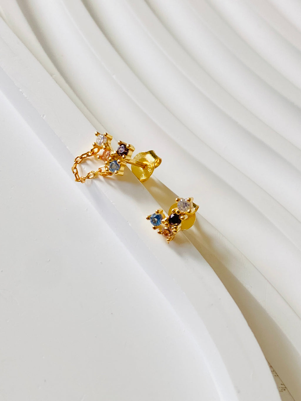 Side view of asymmetric multicolour stud earrings showing gold posts