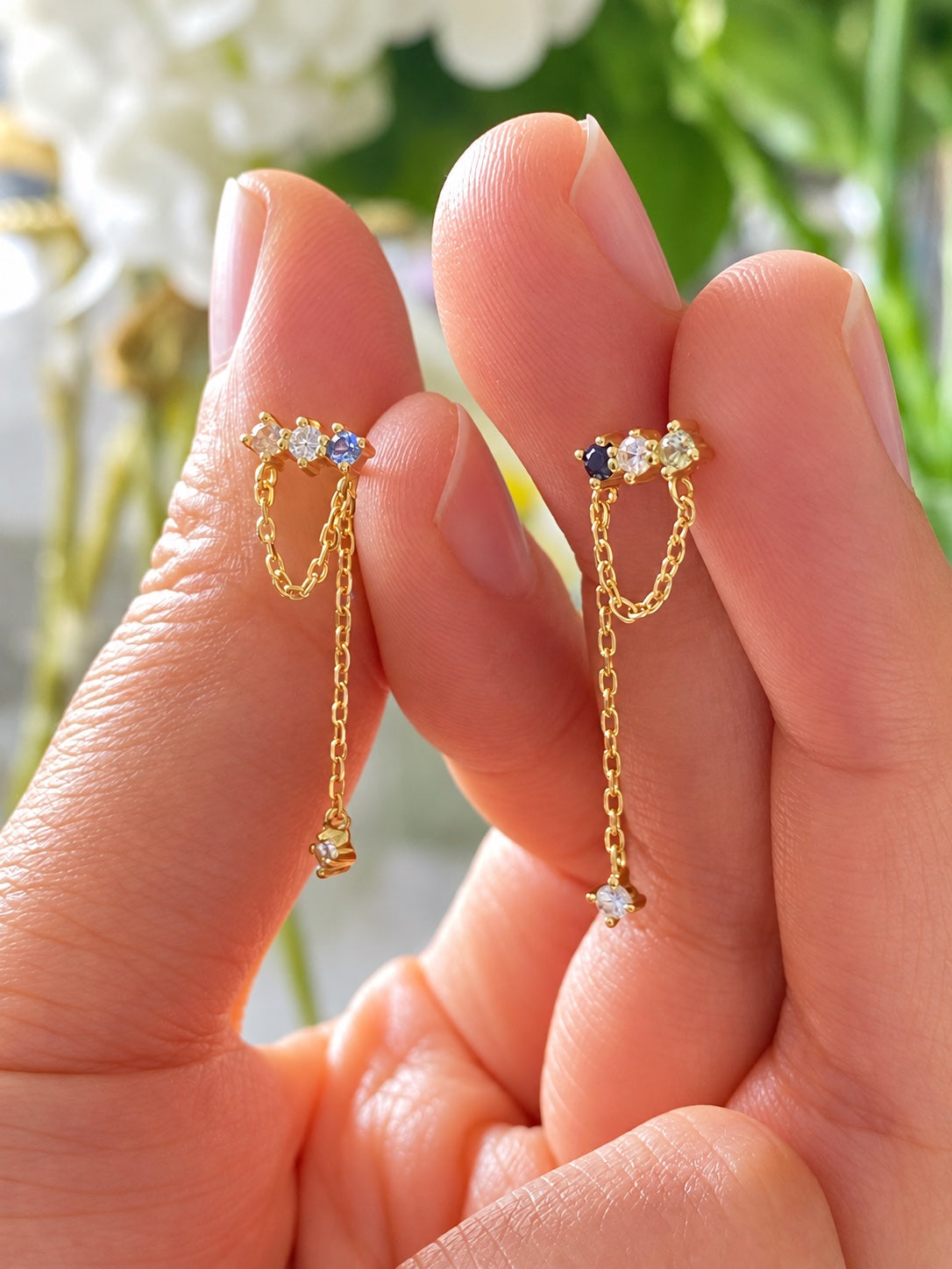 Pair of colourful gold chain drop earrings held between fingers for scale
