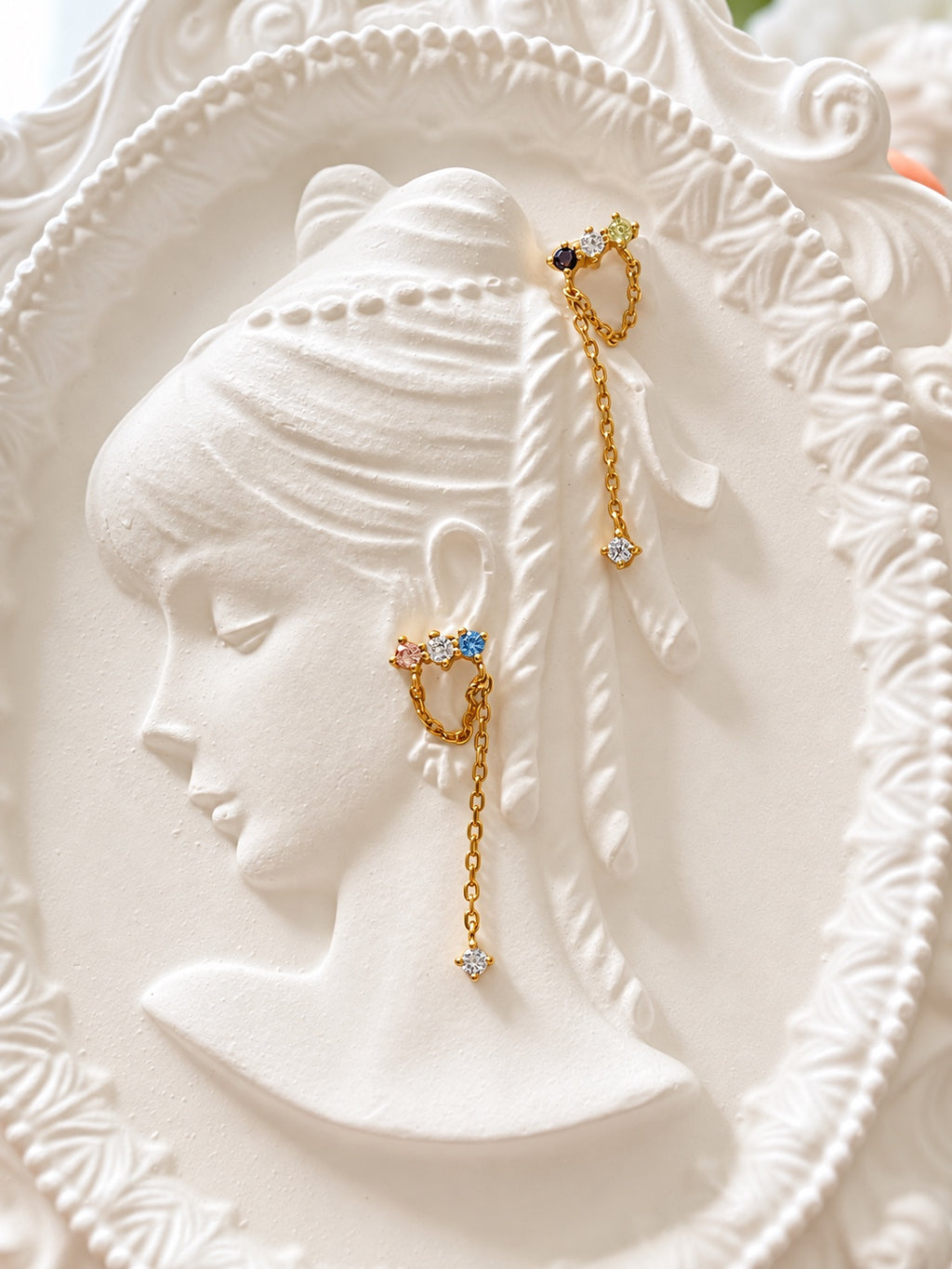 Asymmetric chain drop earrings displayed on an ivory relief